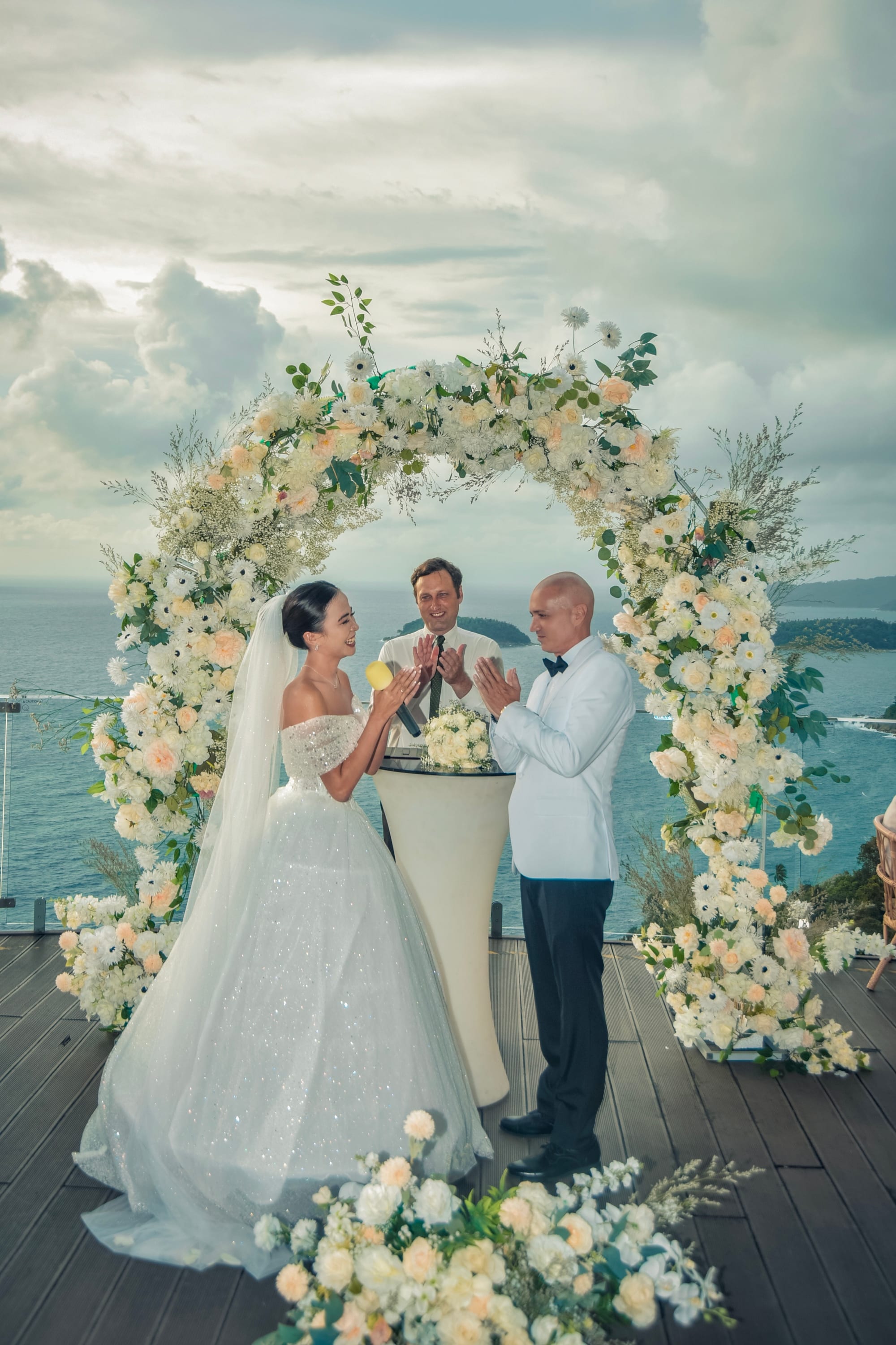 Wedding vow exchange under a floral arch overlooking the Andaman Sea